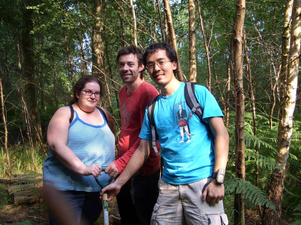 A woman and two men holding a shovel in a wood