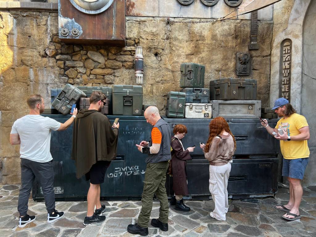 People standing in front of cargo boxes, looking at their phones and scanning objects