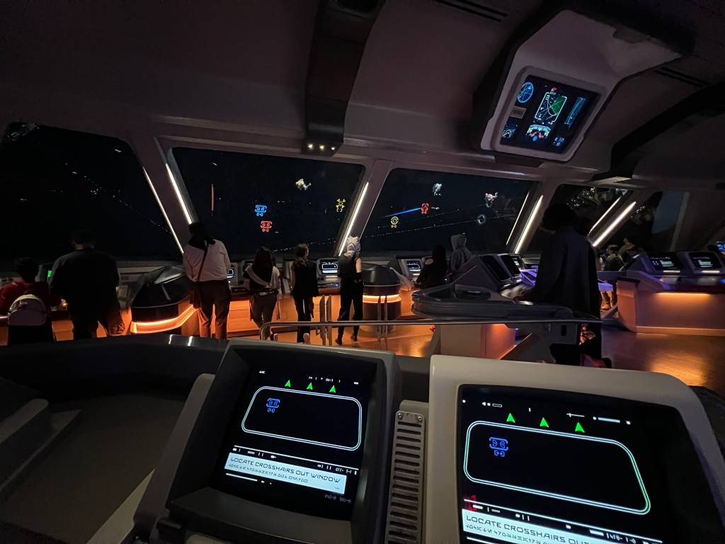 A computer screen with a blue reticle, looking out onto a big viewscreen with lots of differently-coloured reticles