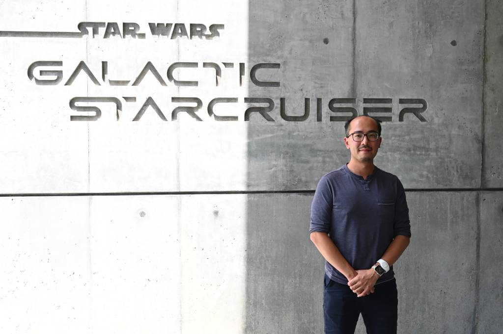 Adrian in front of a sign saying Star Wars: Galactic Starcruiser outside, in normal clothes