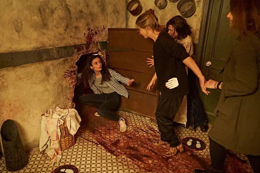 A woman crouches into a hole in a wall behind some shelves