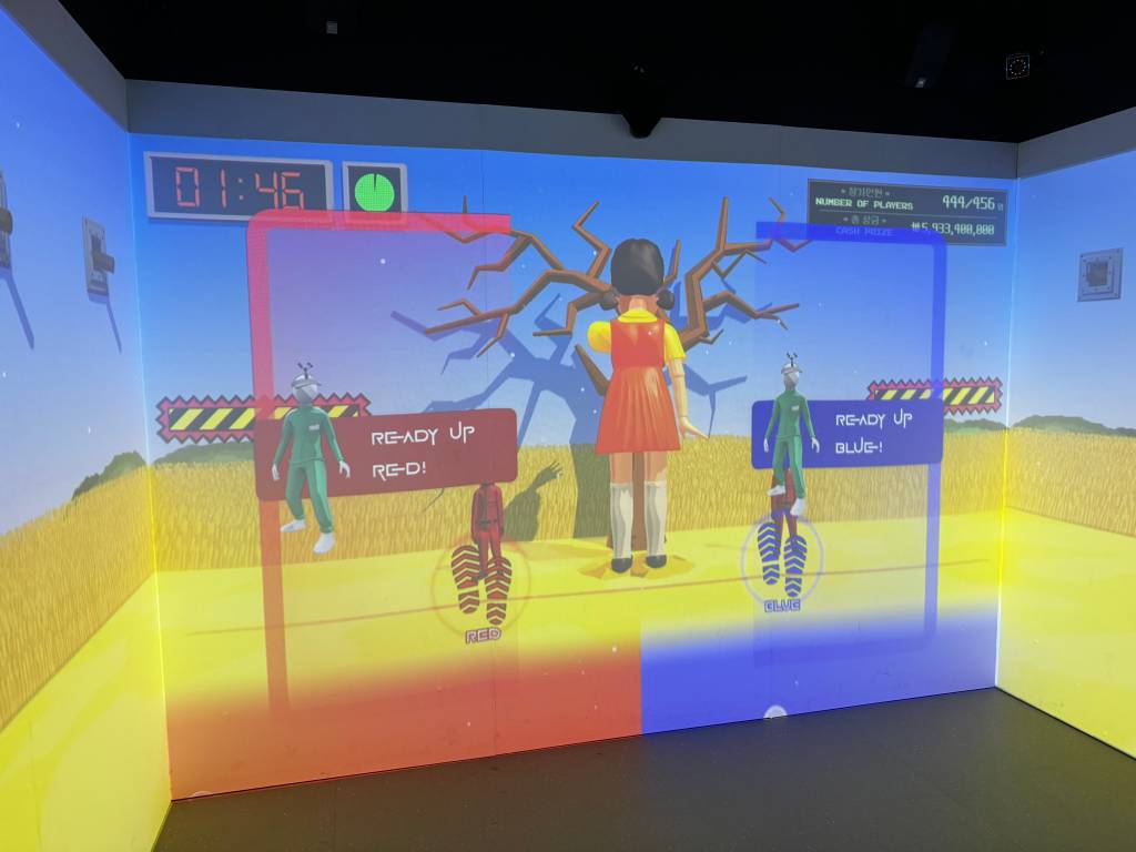 A giant girl faces away from us. A sign has "Ready Up Red!" and "Ready Up Blue!"