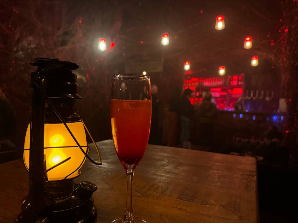 A red cocktail sitting next to an old-school lamp in a dark bar