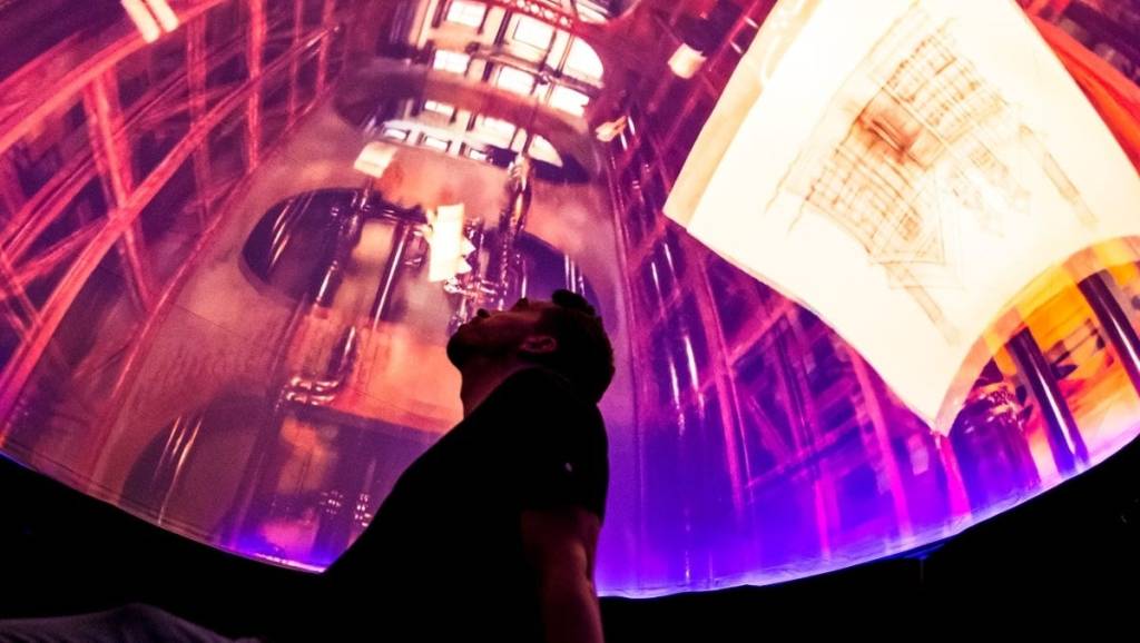 A man stares up at a hemispherical dome projection showing a complex building