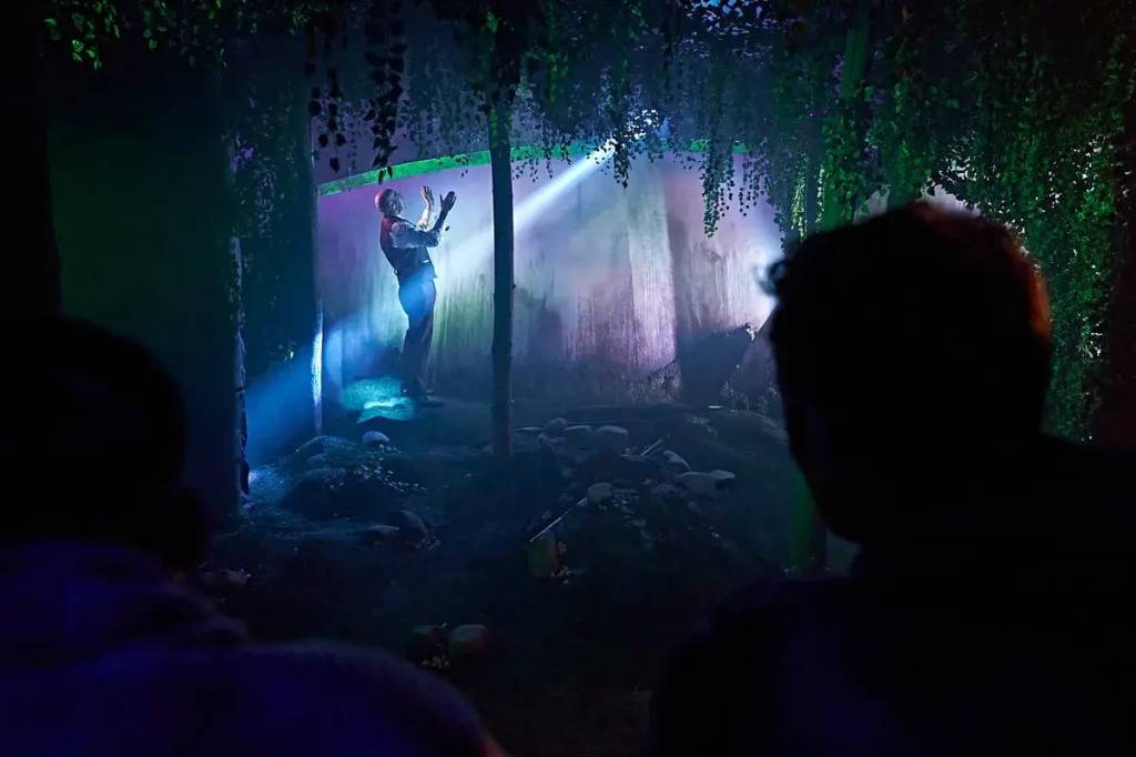 A man stands in front of a facade painted to look like a metal egg. He is targeted by a spotlight.