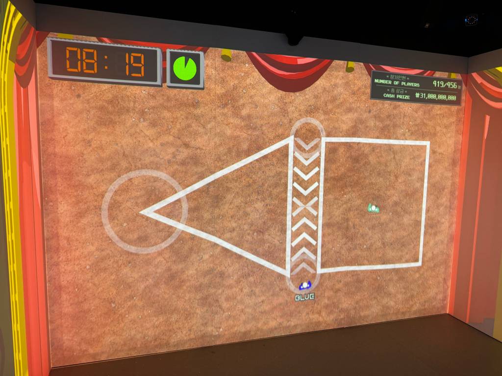 A playing field viewed from above. The blue player is walking through an arrow-marked area while an enemy stands to the right