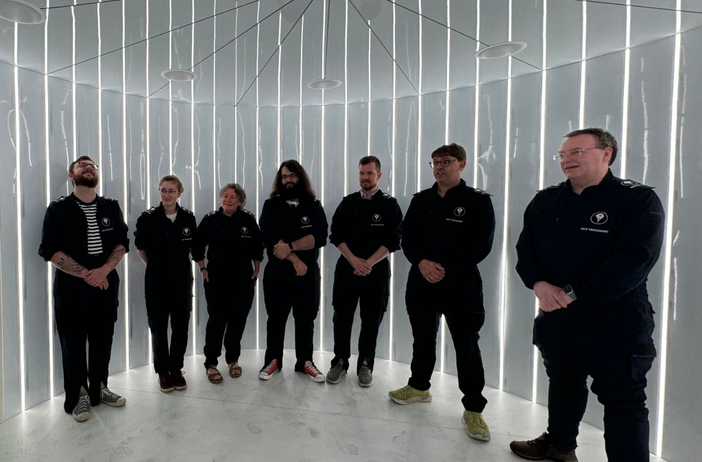 People stand in a circular white room, lined with light bars
