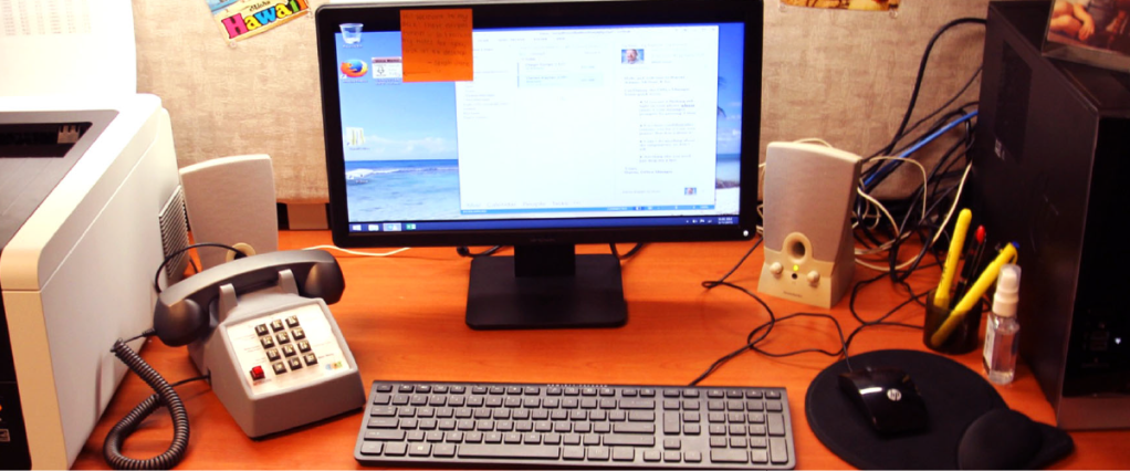 A desktop computer on a desk with old fashioned telephone