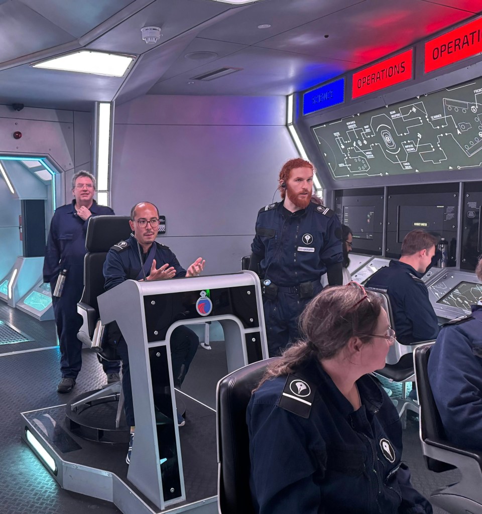 Adrian sitting at the captain's chair, talking to someone on a view screen