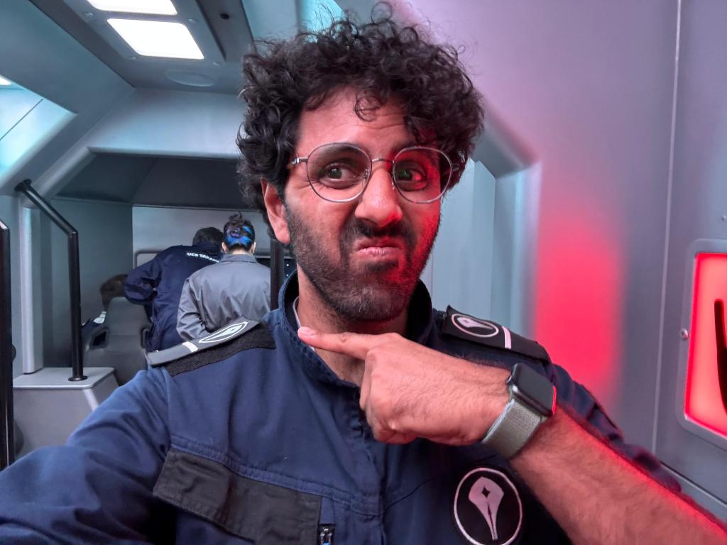 A man with a doubtful face points at a woman in the background