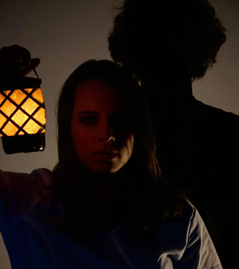 Two people silhouetted against a dark background, one holding a lantern