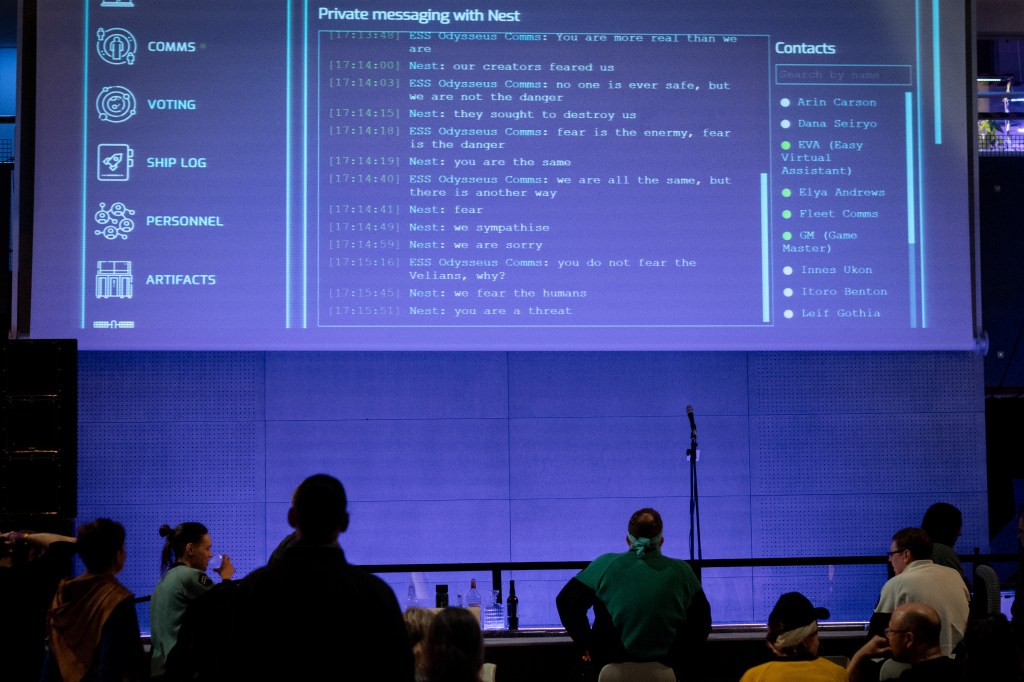A projector shows a text messaging chat between Odysseus and "Nest". People watch from underneath.