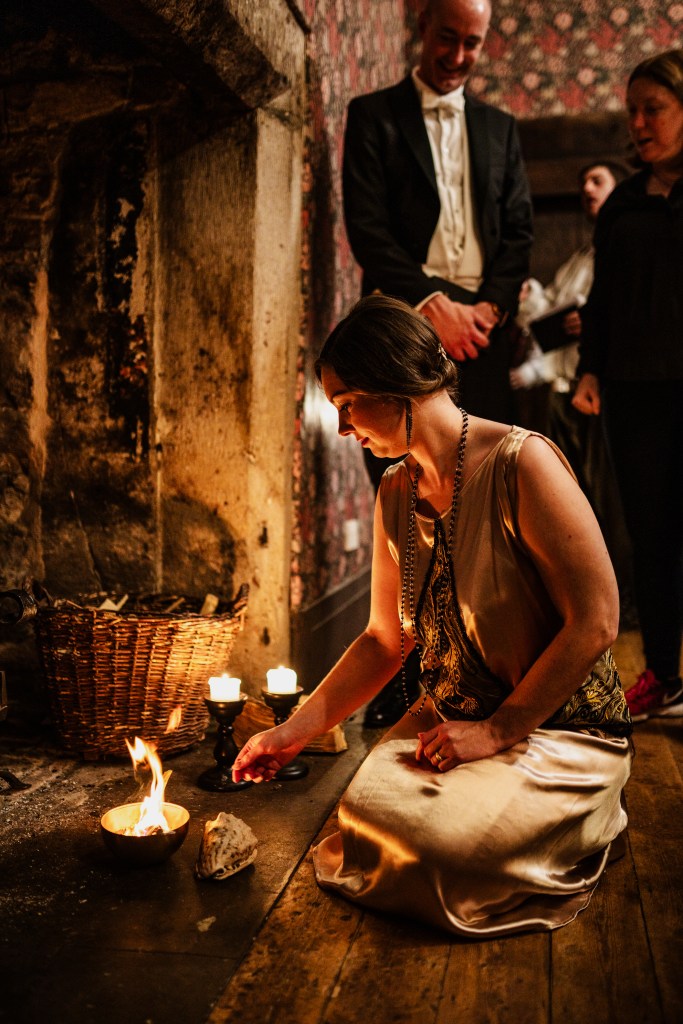 A women in a dress burns paper in a fireplace as others look on