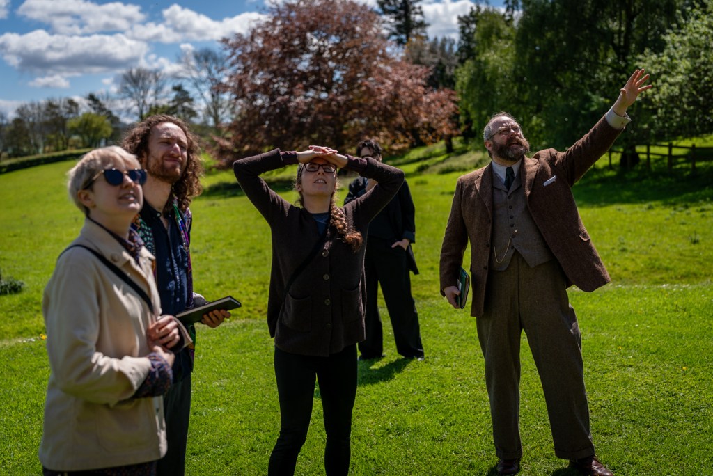 Five people outside on a sunny day looking up at something