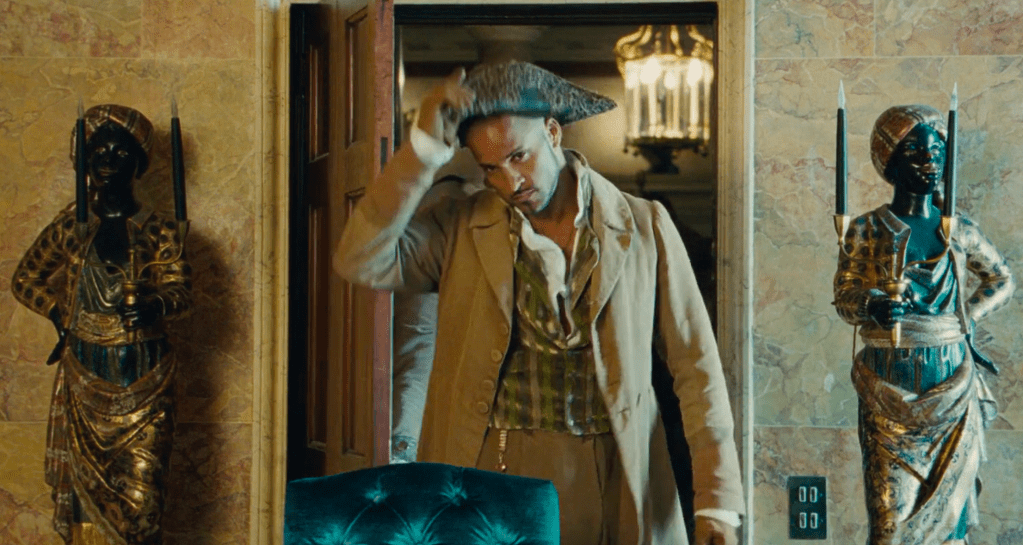 A man enters a room in a coat and a tricorn hat