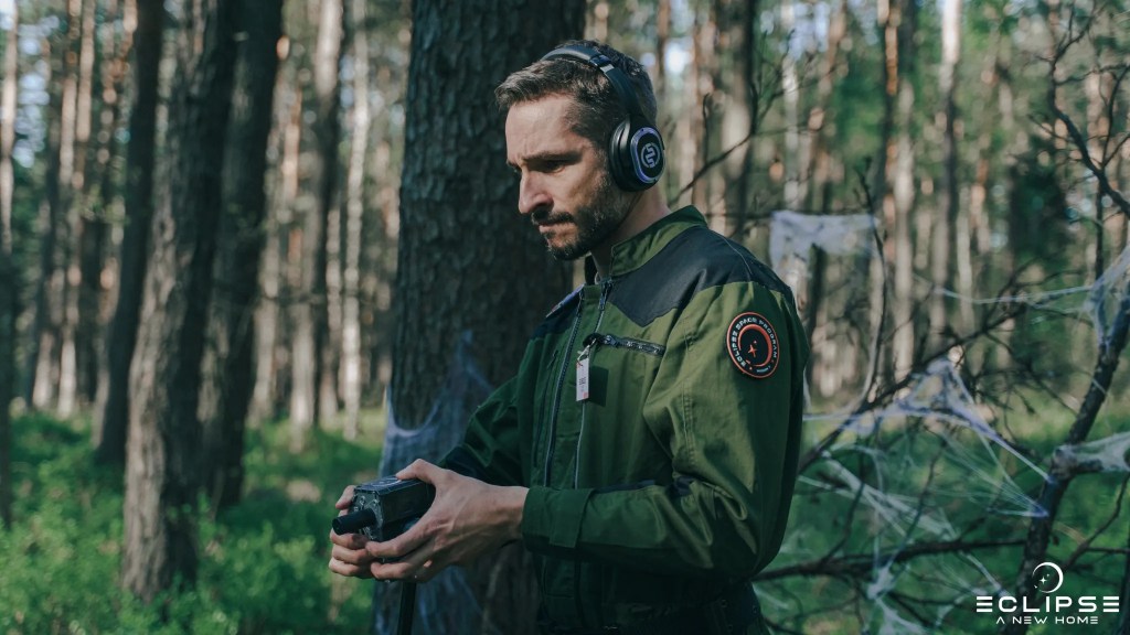 A man in a sci-fi jumpsuit in a forest, aiming a science-fiction like device