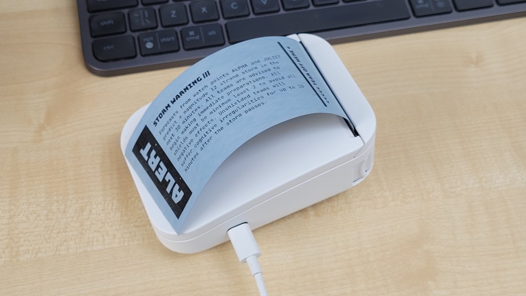 A small white thermal receipt printer with paper coming out reading in bold letters "ALERT"