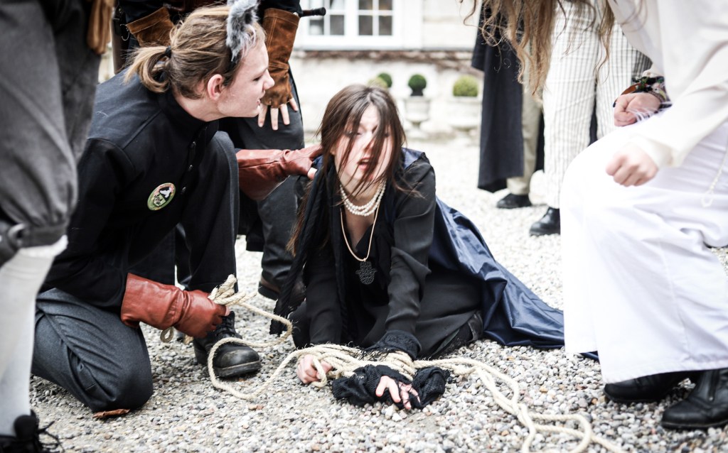 A student on the ground, their hands tied with rope