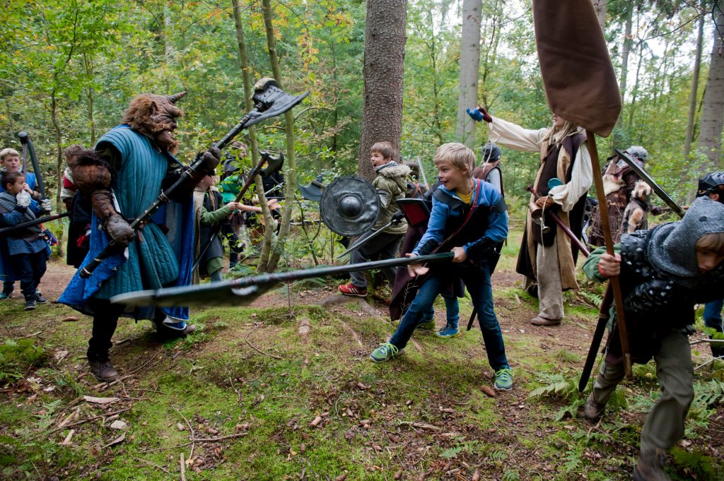 Children in fantasy clothes with large weapons in a forest, fighting monsters