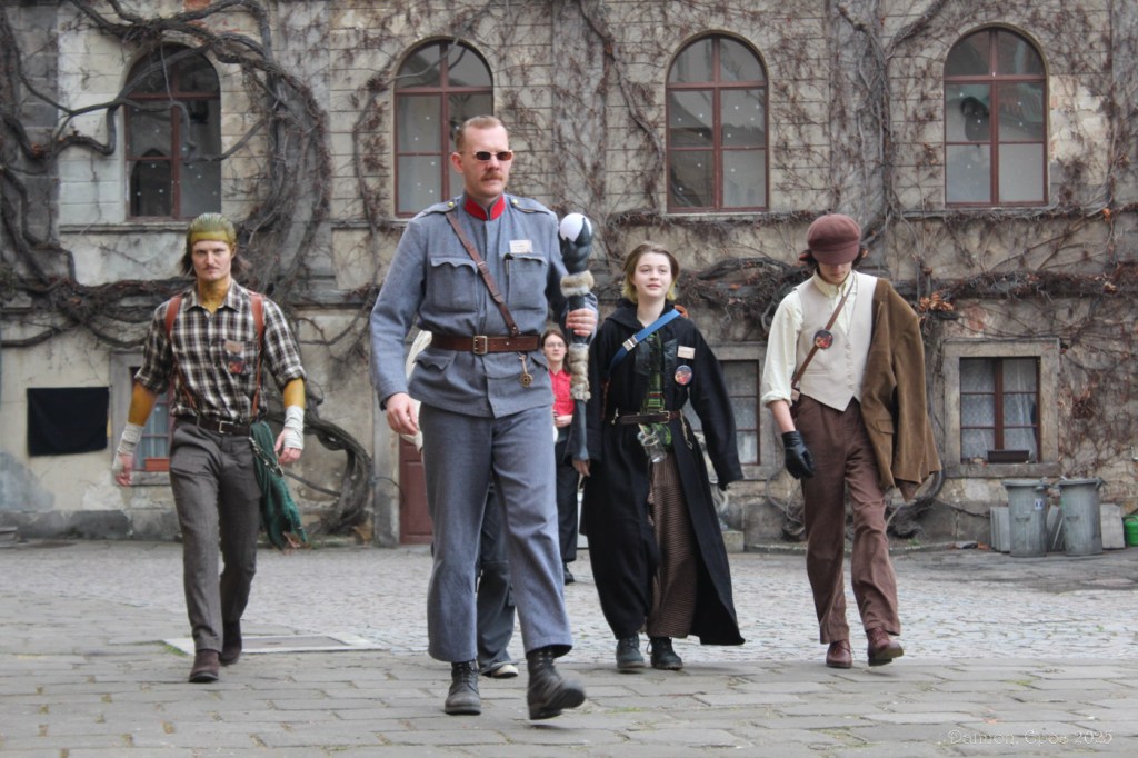 A man in a military uniform marching across a courtyard with people in period clothes following behind