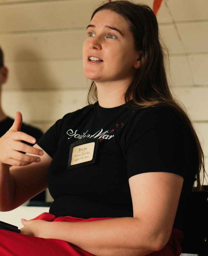A woman gesturing, with long hair and a black t-shirt