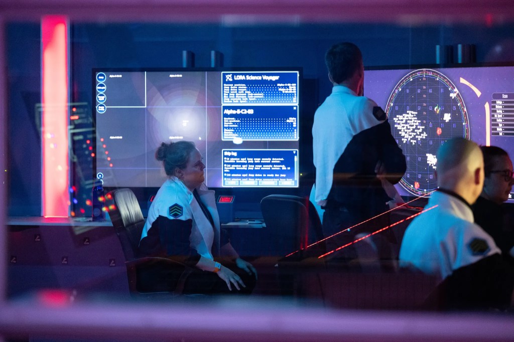 People in a spaceship command centre looking at big screens with space maps