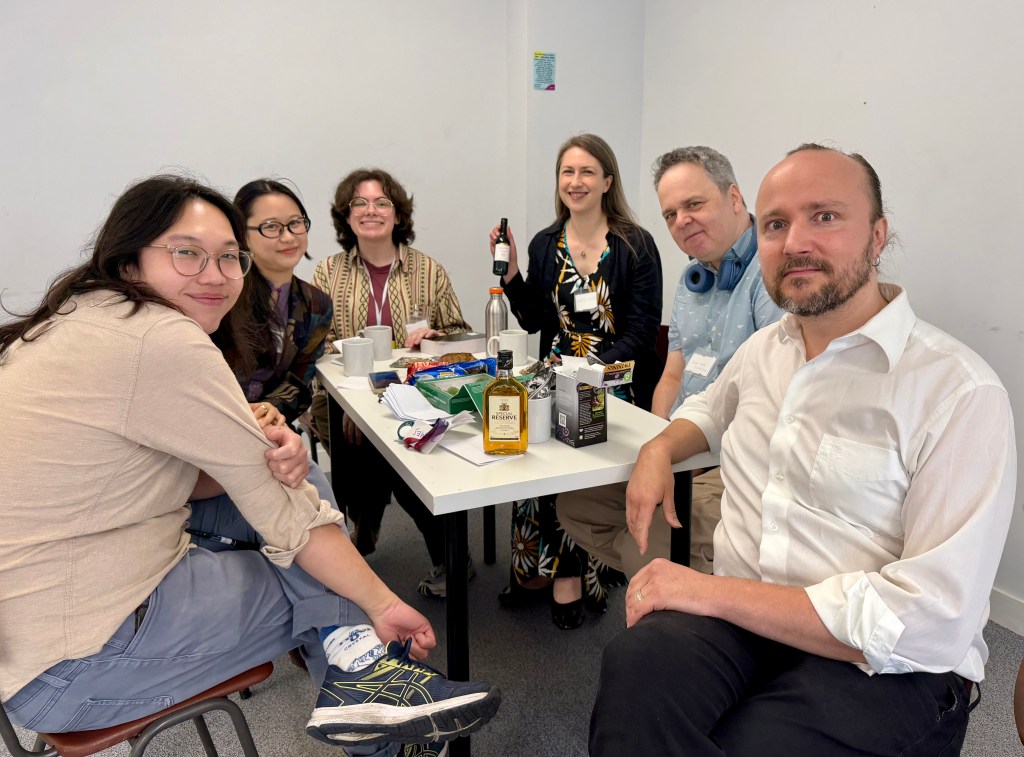 Six people sitting around a table and smiling, with lots of drinks and props on the table