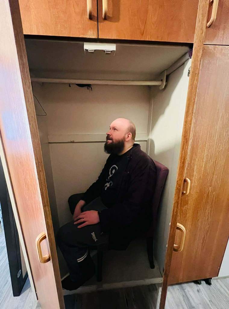 A man sitting in an empty closet on his own
