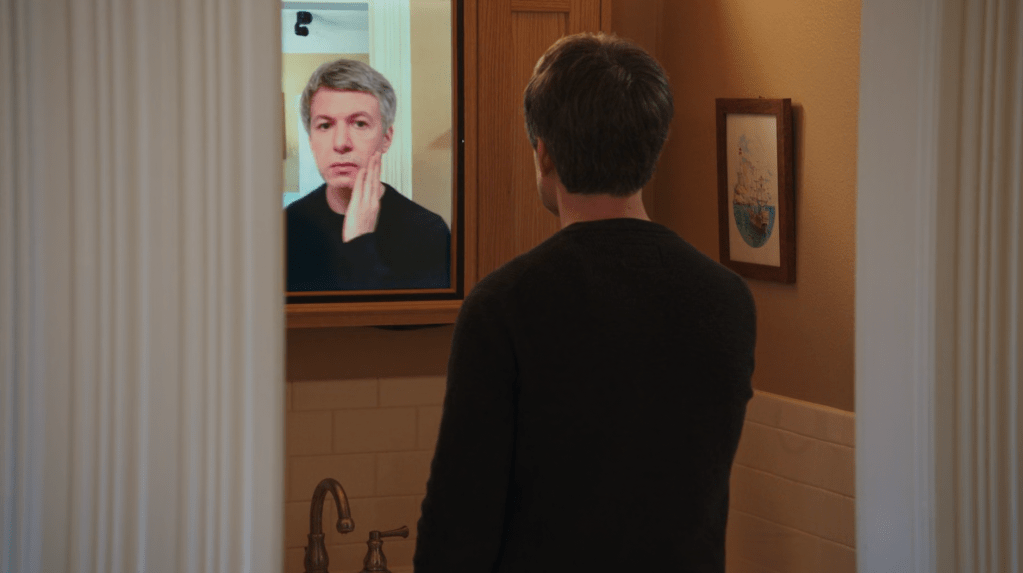A man staring into a "mirror" (actually a digital screen) that's making him look older